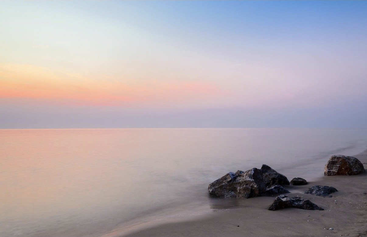 Calm shoreline at sunrise in soft pastel light